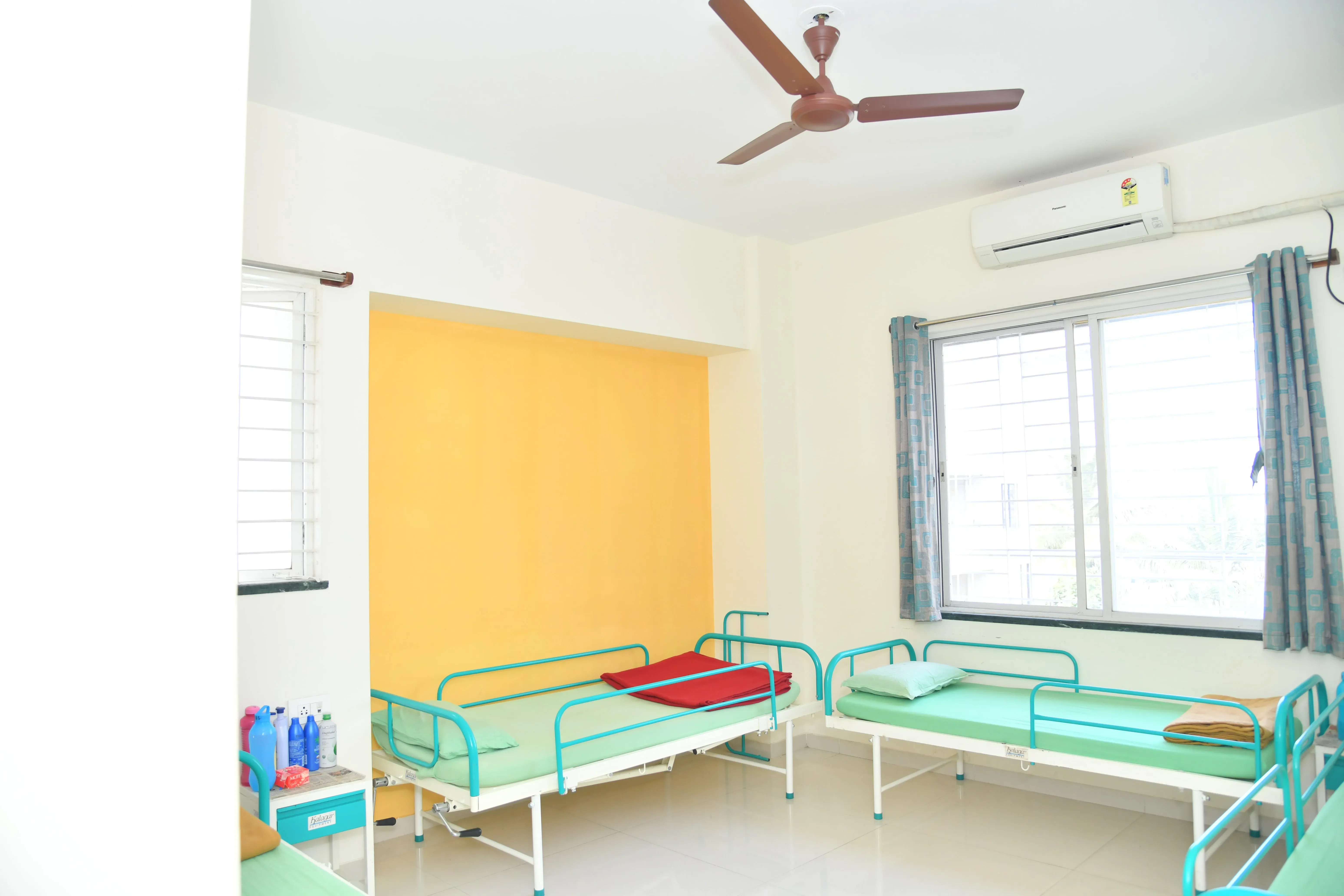 A bright resident room at Satyak with beds, a window and air conditioning